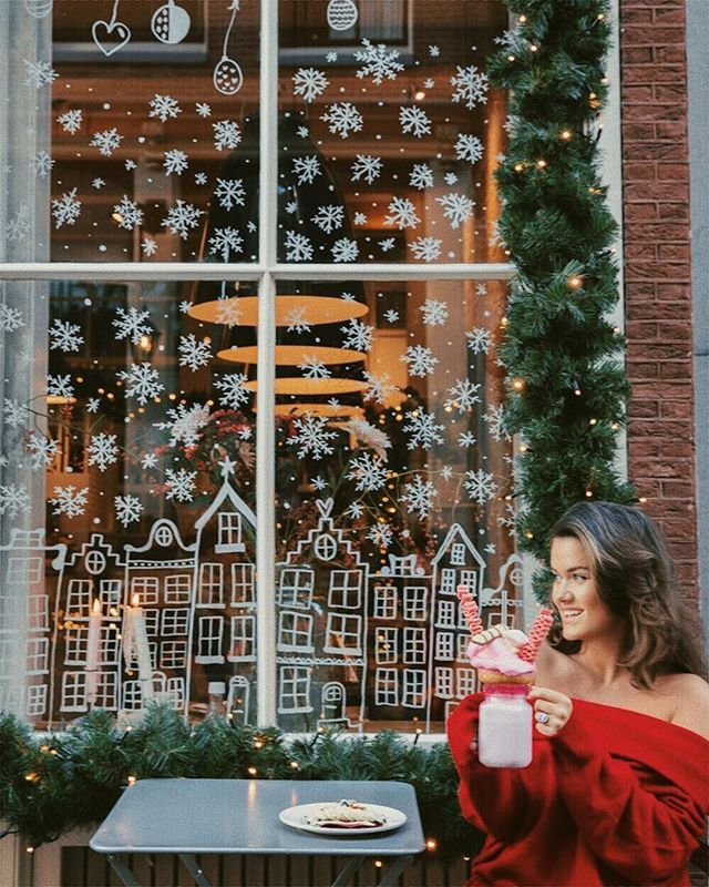 a woman standing in front of a window holding a drink