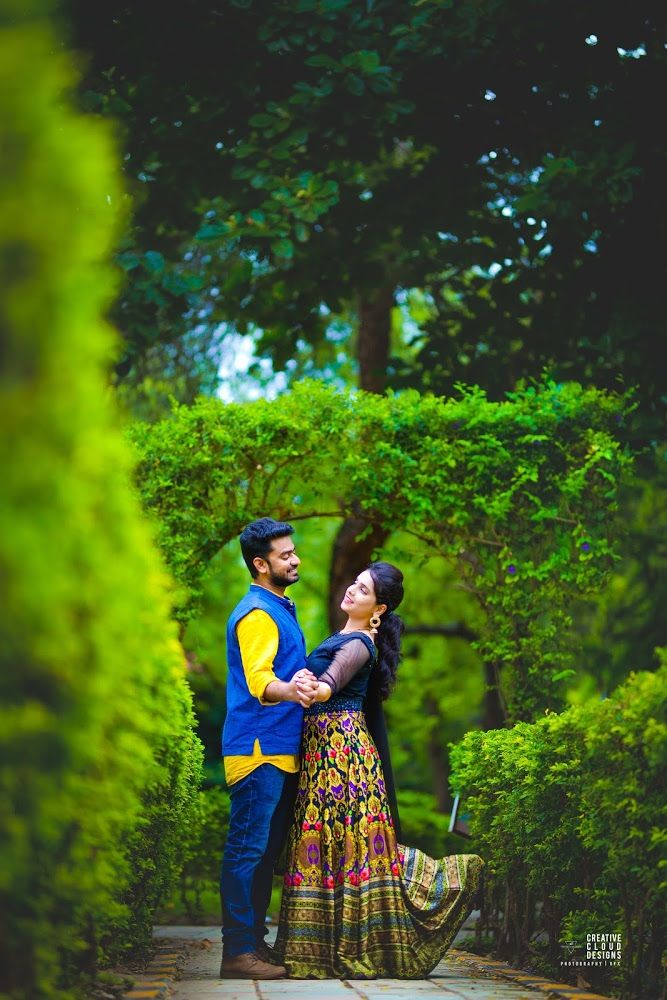 a man and woman standing next to each other in front of some trees with their arms around each other