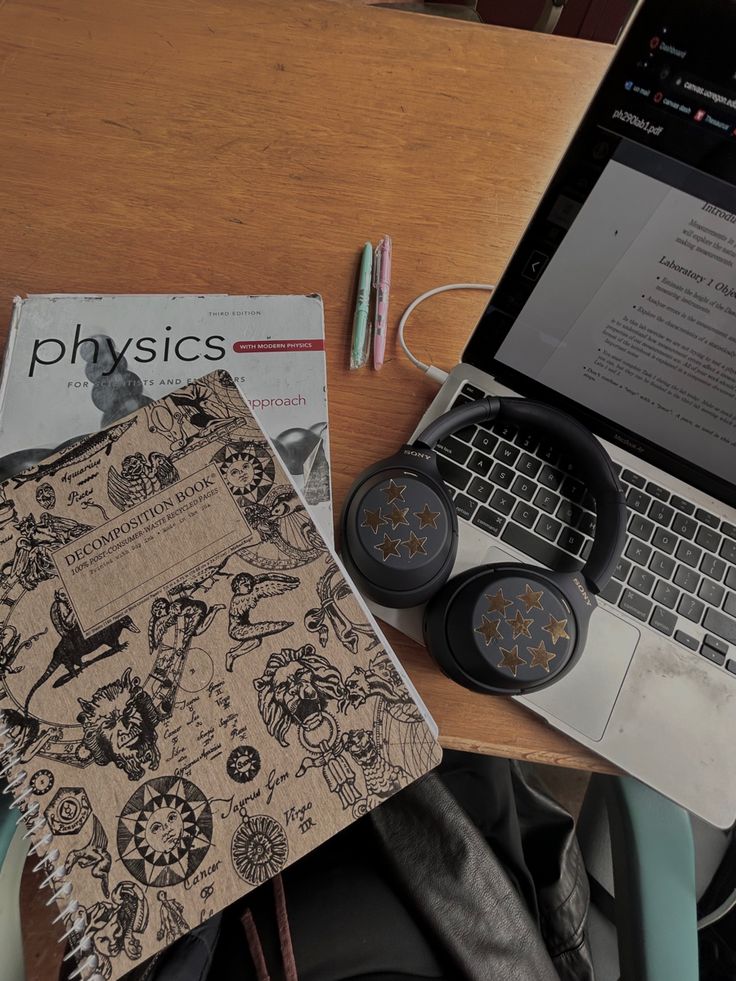 an open laptop computer sitting on top of a wooden desk next to a book and headphones