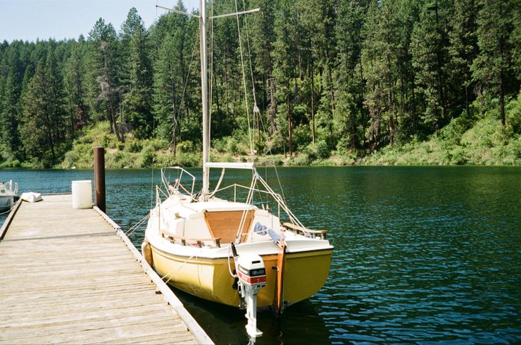 a yellow boat is docked at the end of a wooden dock on a lake with trees in the background