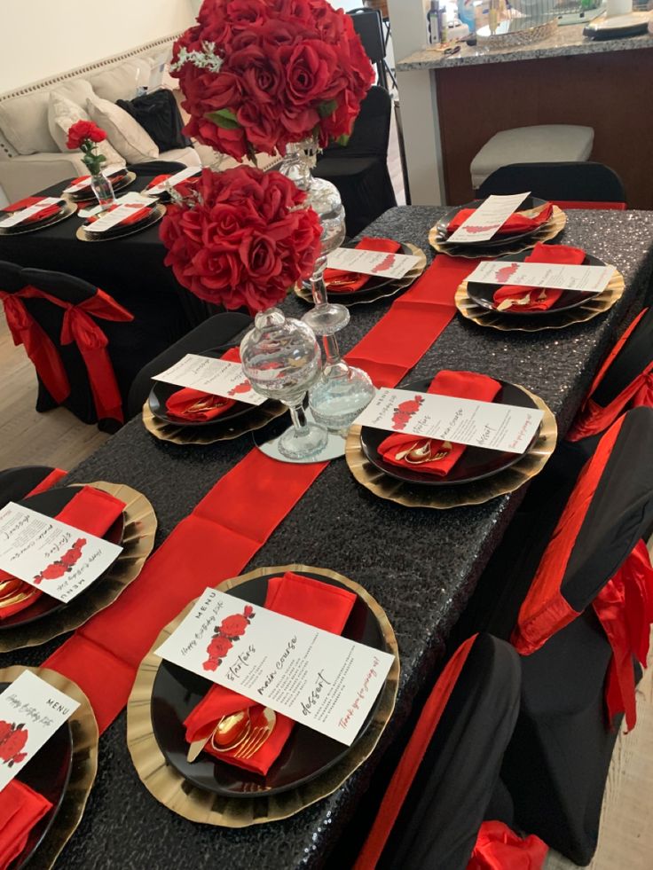 the table is set with red roses and black linens for an elegant dinner party