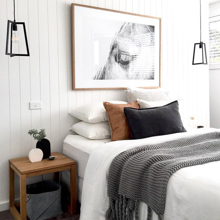 a bed with white sheets and pillows in a bedroom next to a wooden side table