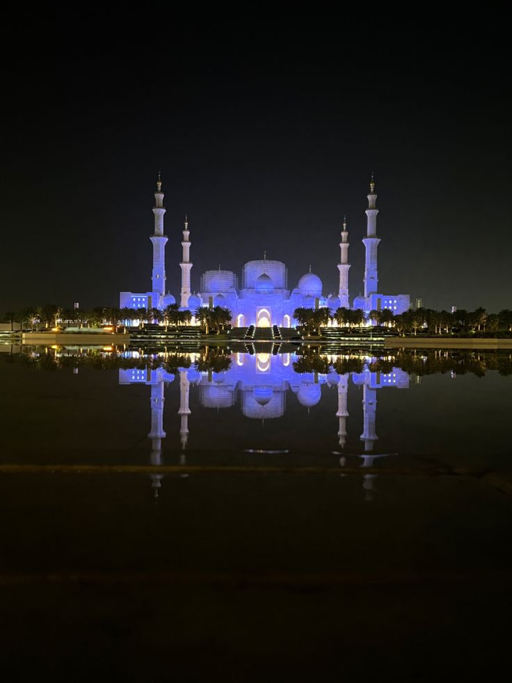 a large building lit up at night with lights on it's sides and reflecting in the water