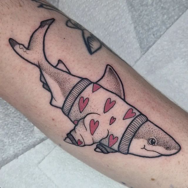 a man's arm with a tattoo of a shark wearing a sweater and hearts on it