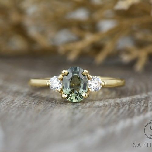 an oval green and white diamond ring on top of a piece of wood with grass in the background