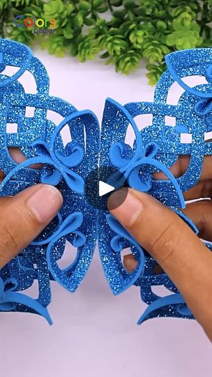 two hands are holding blue plastic bows with glitter on them and one hand is pointing at the bow