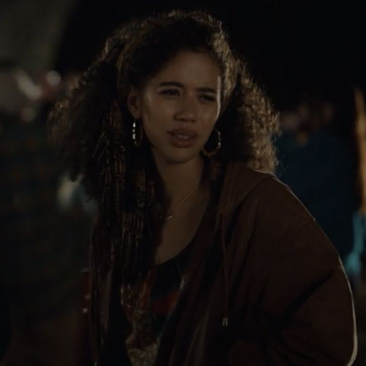 a woman with long braids standing in the dark, looking off to her right