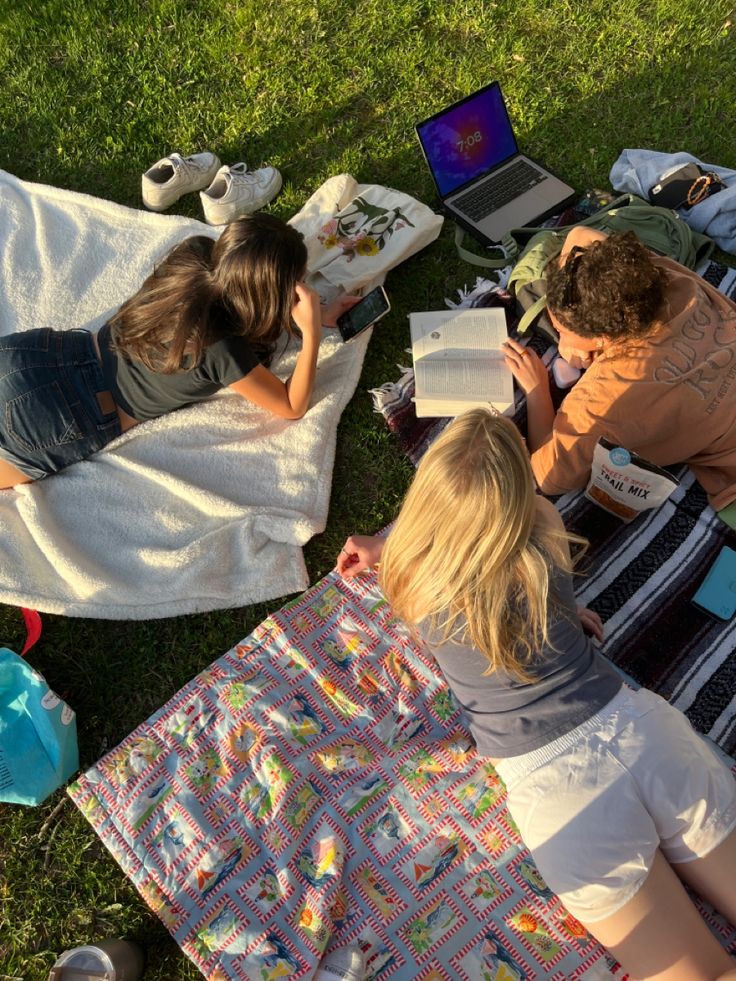 three people sitting on the grass reading books