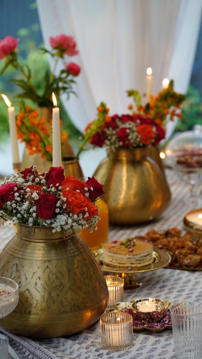 a table topped with gold vases filled with red flowers and candles next to plates