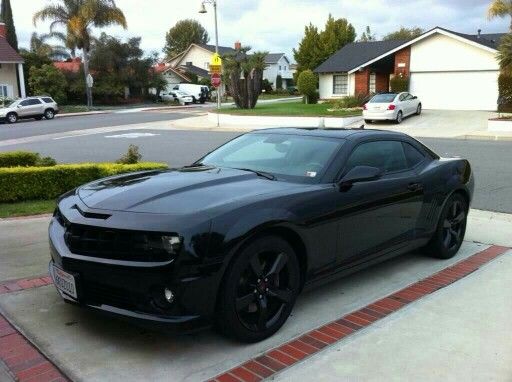 a black chevrolet camaro parked in front of a house