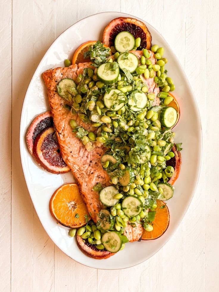 a white plate topped with salmon, cucumbers and oranges