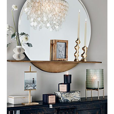 a shelf with candles and pictures on it in front of a round mirror over a dresser