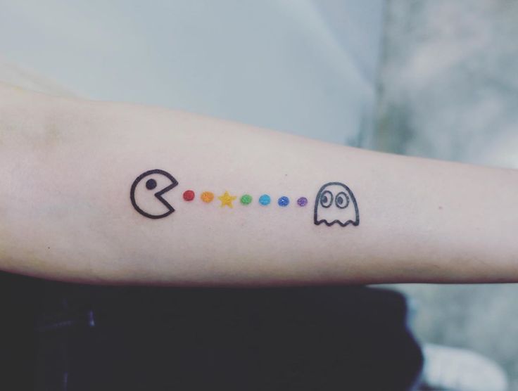 a person's arm with a pacman and ghost tattoo on the left forearm