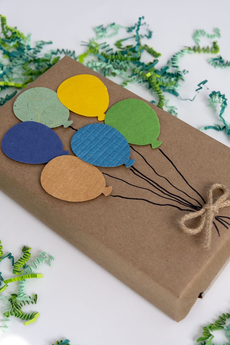 a brown box with balloons on it and some string attached to the top, sitting on green leaves