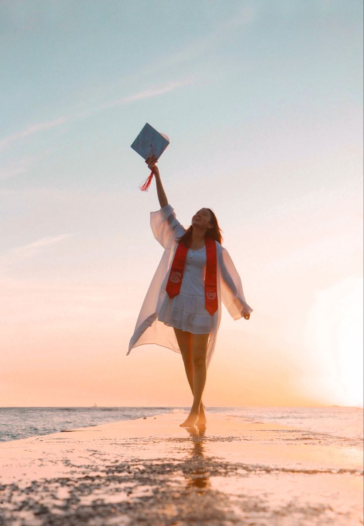 a woman is walking on the beach with her graduation cap