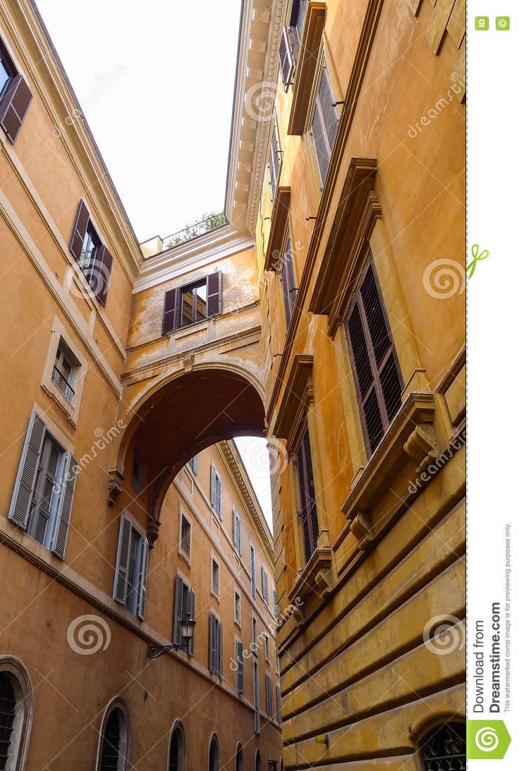 an alleyway between two buildings with arched windows and shutters on either side, looking up at the sky