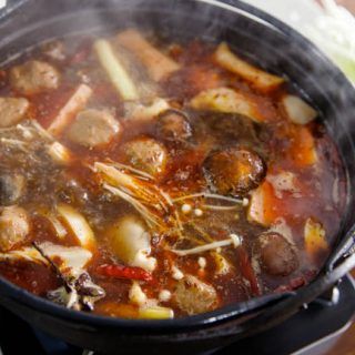 a pot filled with meat and vegetables cooking on top of a stove burner next to a wooden table