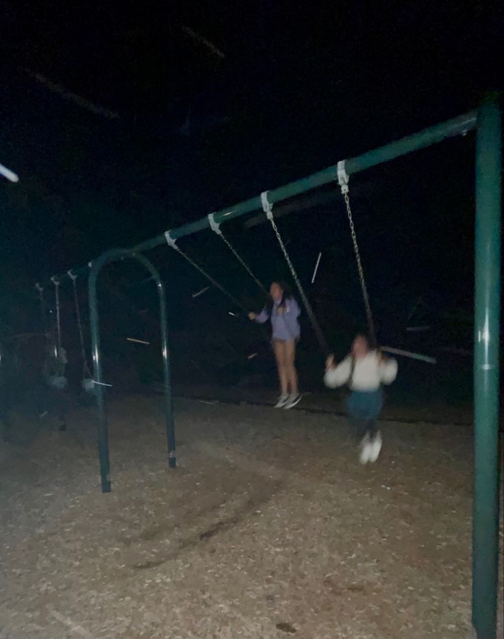 two people playing on swings in the dark