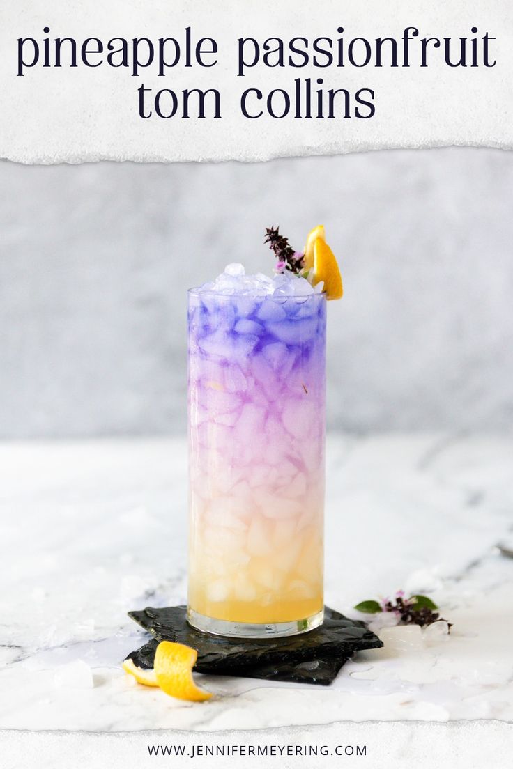 a tall purple and yellow drink sitting on top of a white table next to lemon wedges