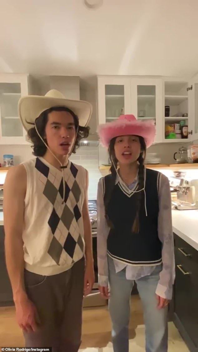 two young people standing in a kitchen with hats on their heads and one wearing a sweater