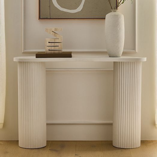 a white vase with flowers sitting on top of a table next to a framed painting