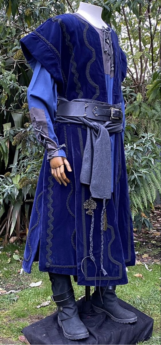 a man dressed in medieval clothing standing on top of a lush green field next to trees