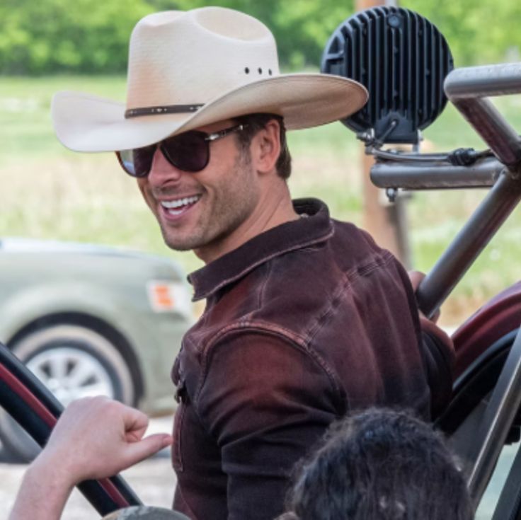 a man wearing a cowboy hat and sunglasses sitting in the driver's seat of a car