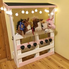 three stuffed animals are on top of a toy horse stand with lights strung from the ceiling