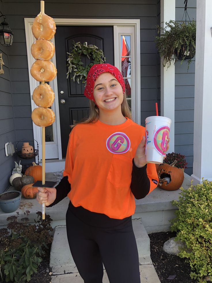 a woman holding a donut and drink in front of a house with halloween decorations