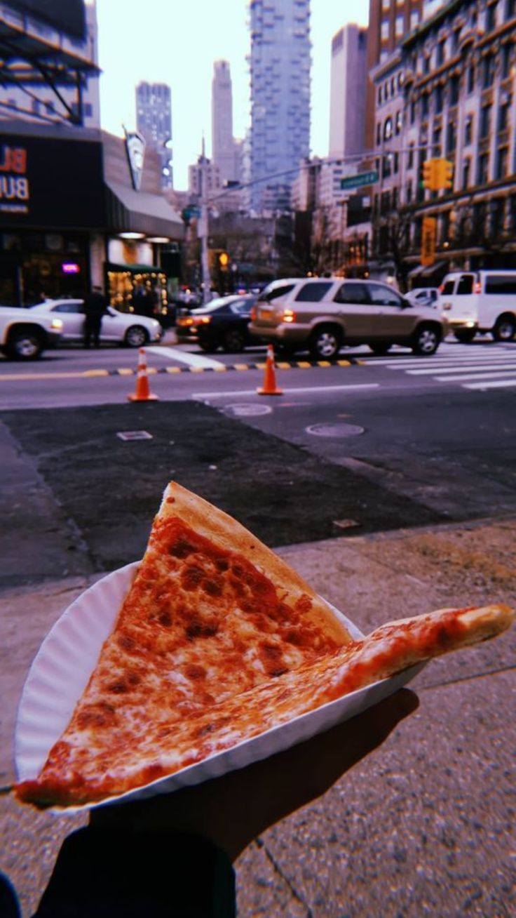 a slice of pizza sitting on top of a paper plate in front of a city street