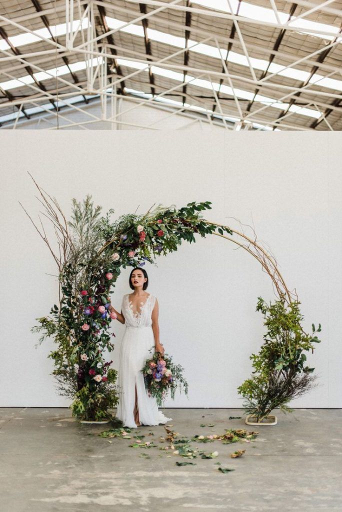 a woman standing in front of a floral arch with greenery and flowers on it