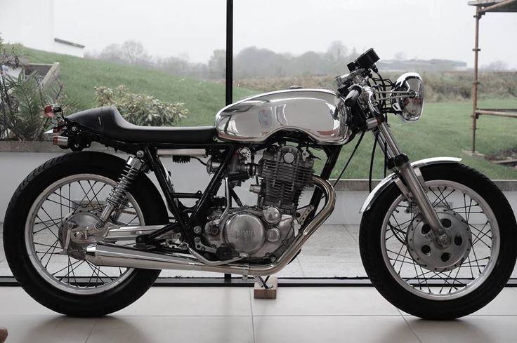 a silver motorcycle parked in front of a window next to a grass covered field and building