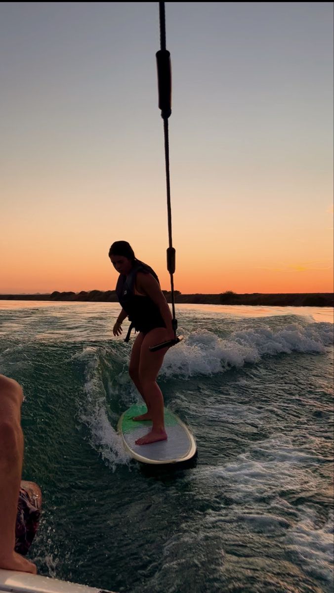 a woman riding a surfboard on top of a wave in the ocean at sunset