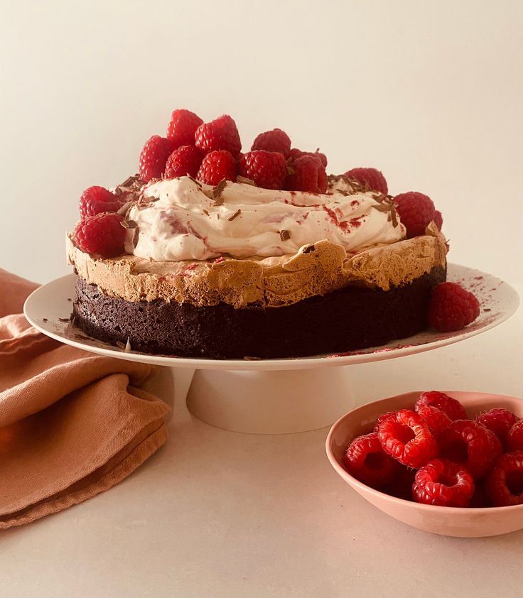 a chocolate cake with raspberries and whipped cream on top, next to a bowl of raspberries