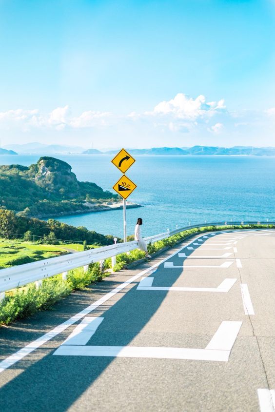 a person standing on the side of a road next to an empty street and ocean