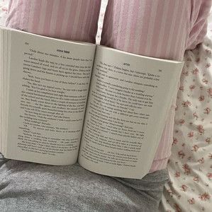 an open book sitting on top of a bed next to pillows and blankets with pink flowers