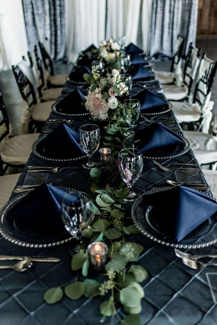 the table is set with black linens, silverware and floral centerpieces