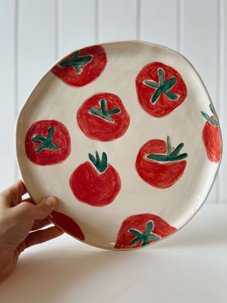 a hand holding a plate with tomatoes painted on it