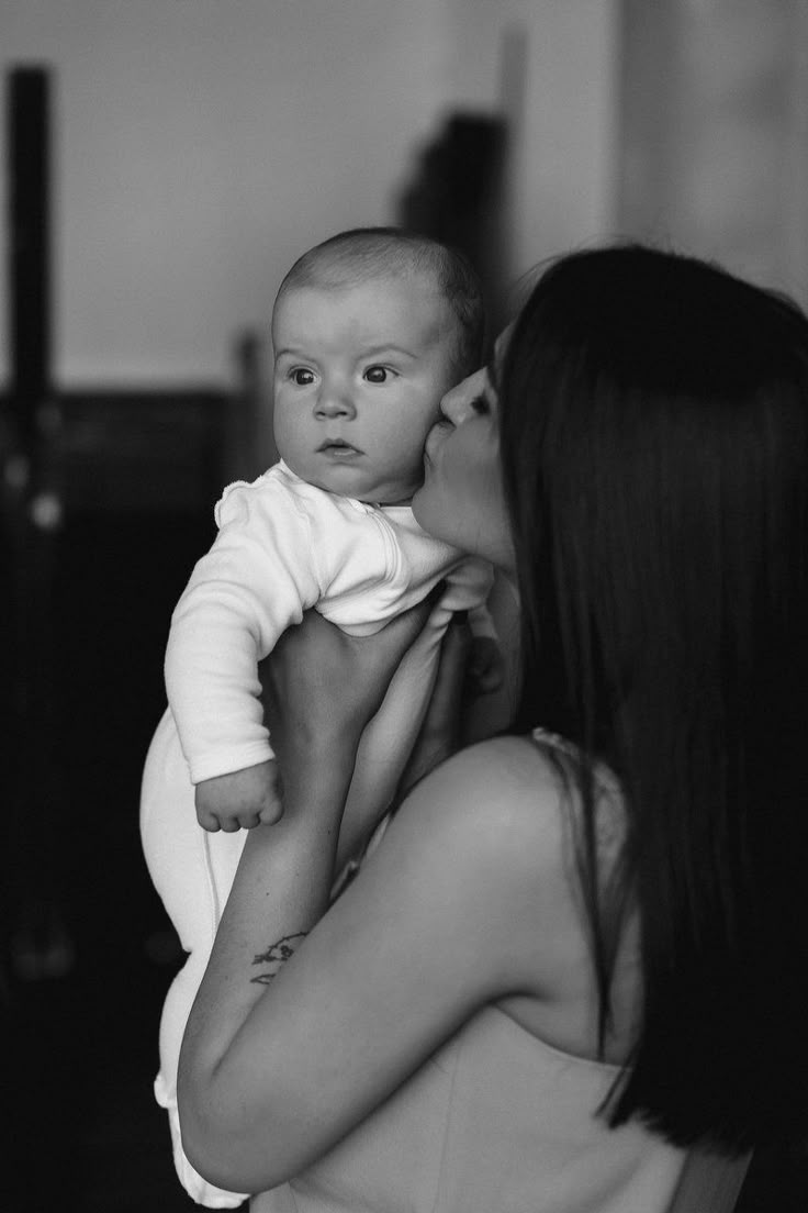 a woman holding a baby in her arms and kissing it's face with the other hand