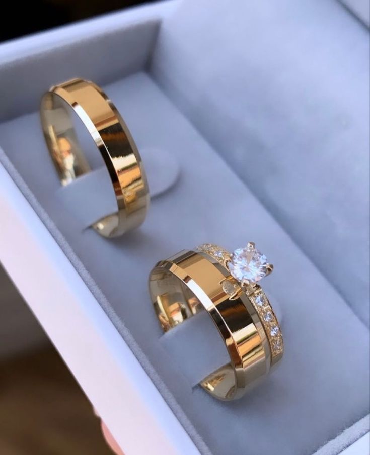 two gold rings in a box with diamonds on the inside, and one has a white diamond