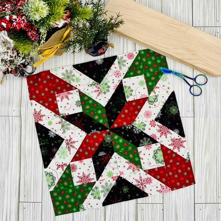 a quilted table topper next to scissors and flowers on a white wooden surface