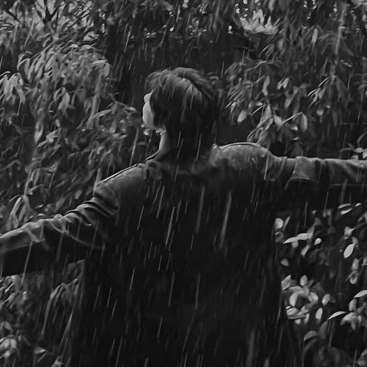 a man is standing in the rain with his arms out and looking at something behind him