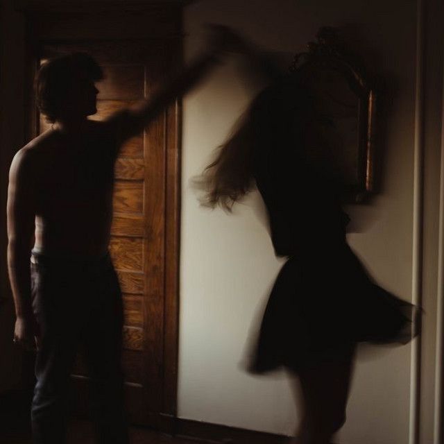 a man standing next to a woman in front of a door with her arms outstretched