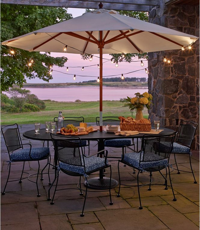 an outdoor dining area with table, chairs and umbrella over looking the water at dusk