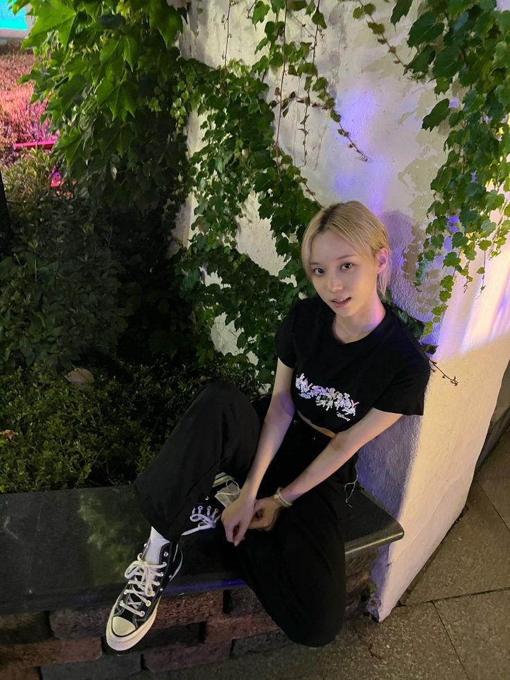 a woman sitting on a bench in front of some plants