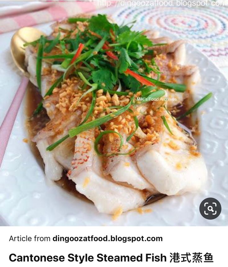 a white plate topped with fish covered in sauce and garnished with veggies