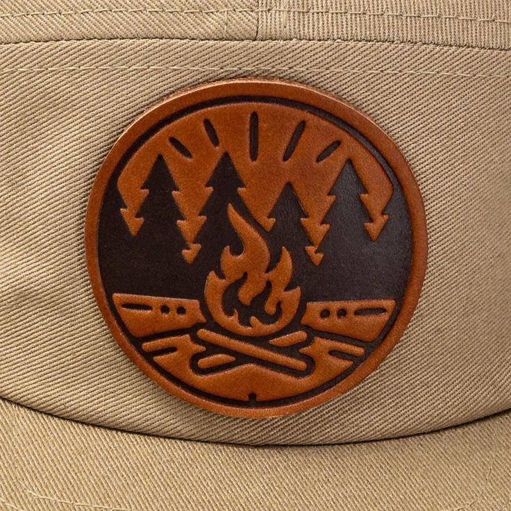 Get Fired Up for Adventure with this Campfire Cap! The patch on this hat features a classic campfire scene, capturing the timeless allure of the great outdoors. It's a simple yet evocative image: two logs ablaze with flames reaching upwards, cradled by a circle that hints at the unity and completeness of nature. The trees standing sentinel on either side anchor the scene in the wild, calling to mind the serenity of the woods and the simple pleasures of a fireside chat under the stars. Each cap i Outdoor Canvas Snapback Hat With Flat Bill, Canvas Snapback Hat For Outdoor Use, Canvas Flat Bill Hat For Outdoor, Outdoor Canvas Hats With Flat Bill, Outdoor Flat Bill Canvas Hat, Outdoor Canvas Hat With Flat Bill, Brown Short Brim Hat For Camping, Outdoor Trucker Hat With Leather Patch And Short Brim, Outdoor Short Brim Hats With Logo Patch