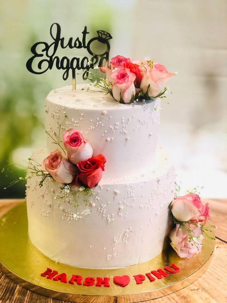 a wedding cake with pink and white flowers on top is sitting on a wooden table