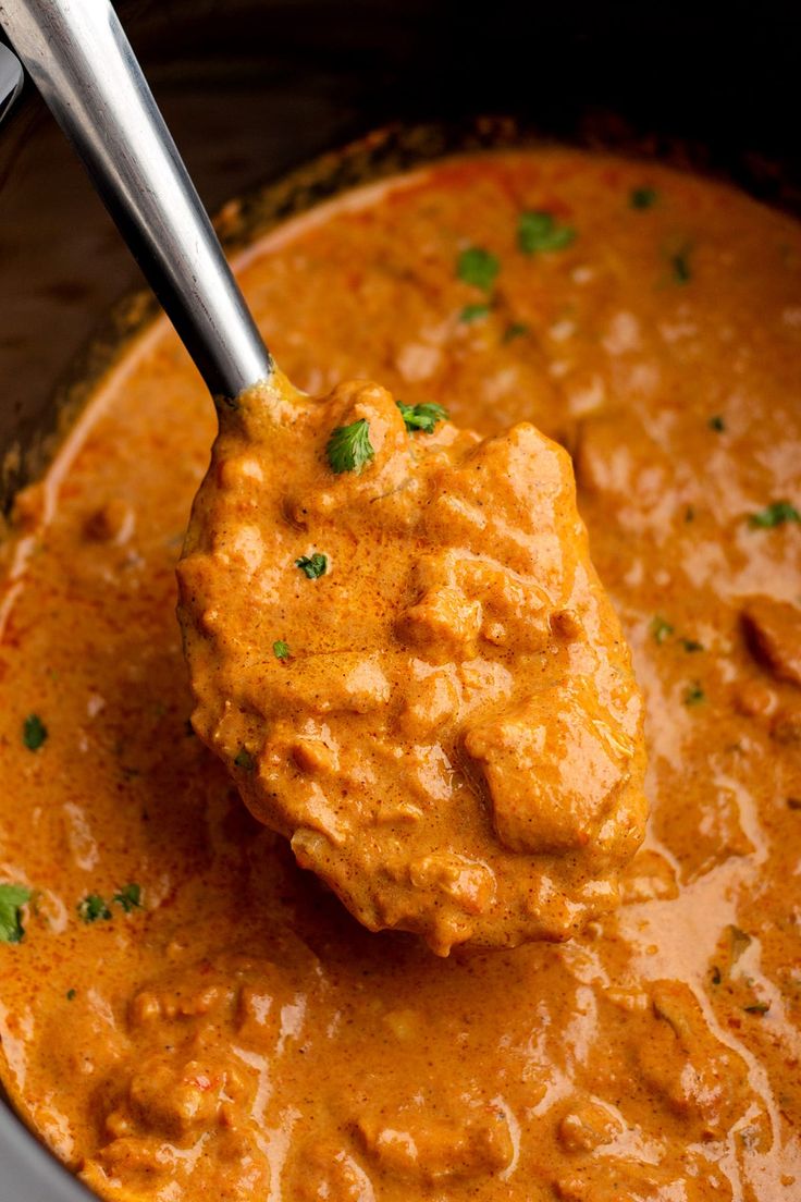 a ladle scooping some food out of a pot filled with red sauce and garnished with parsley