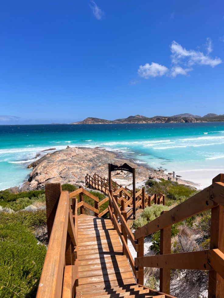 a wooden staircase leading to the beach with clear blue water and white sand in the background